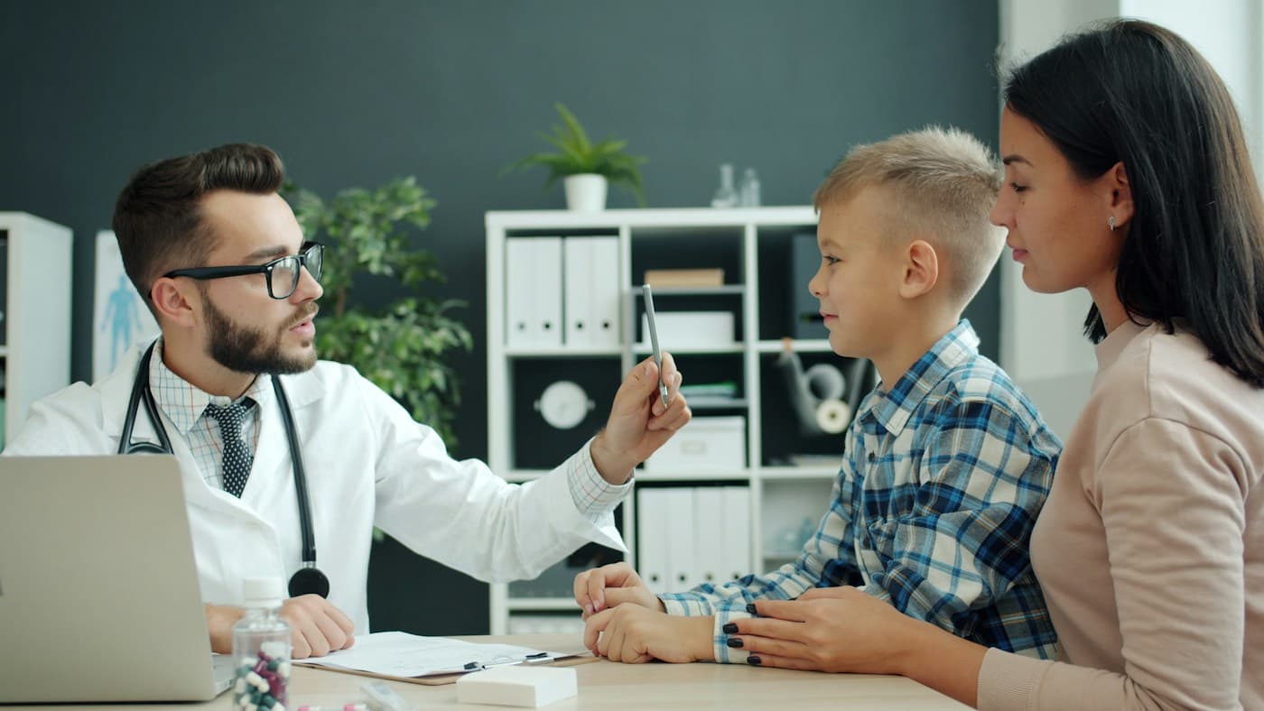 Un pediatra conversa con un niño y su madre durante una consulta.