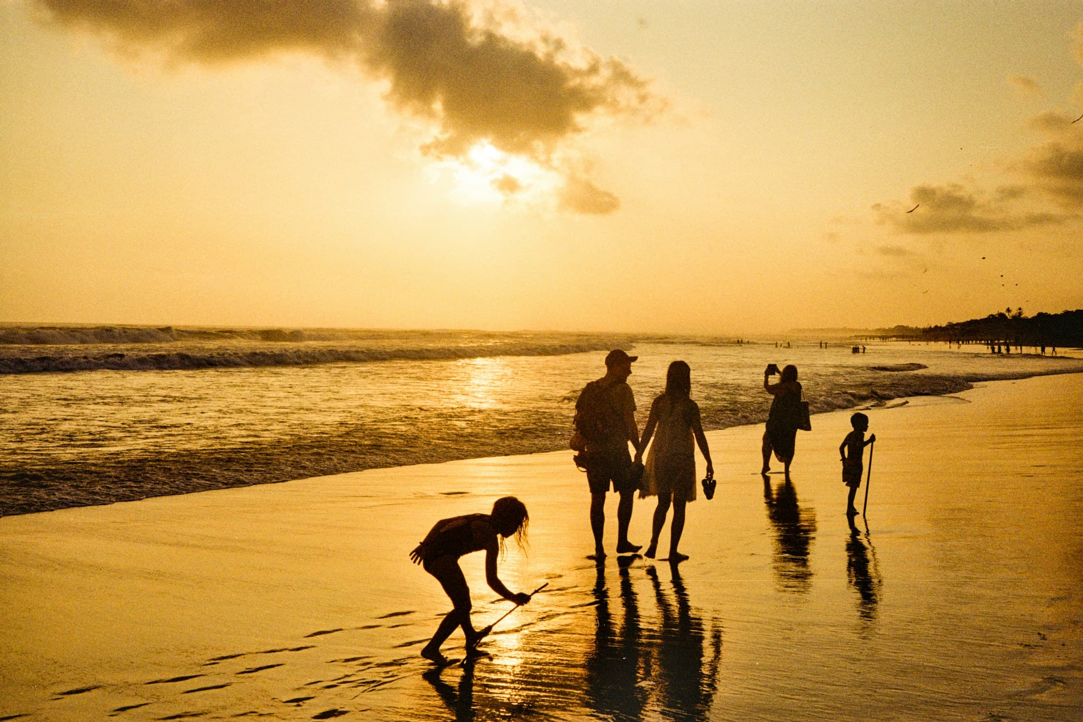 Una familia camina por la orilla de la playa al atardecer.