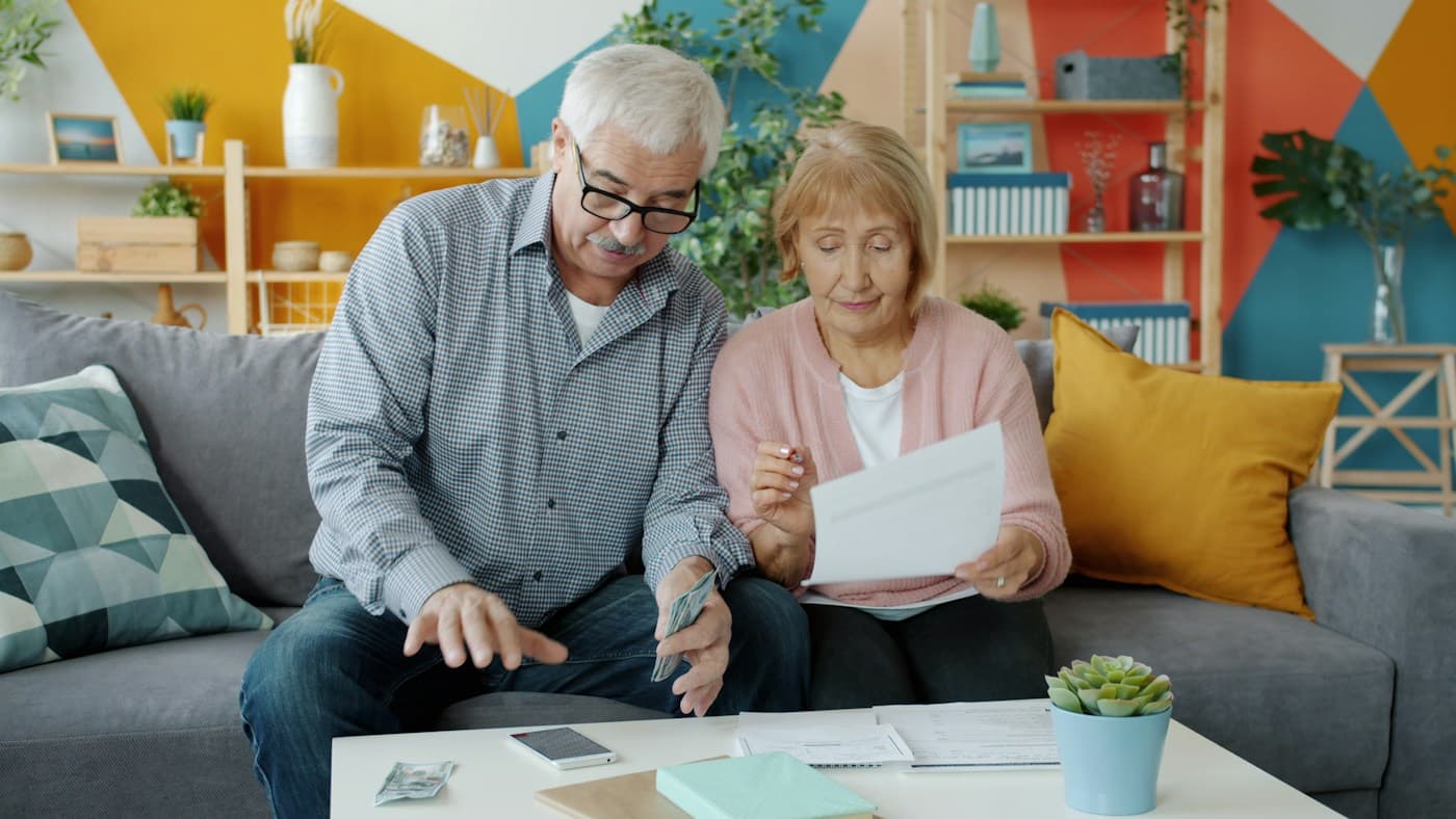 Una pareja de adultos mayores revisa documentos en la sala de su casa.